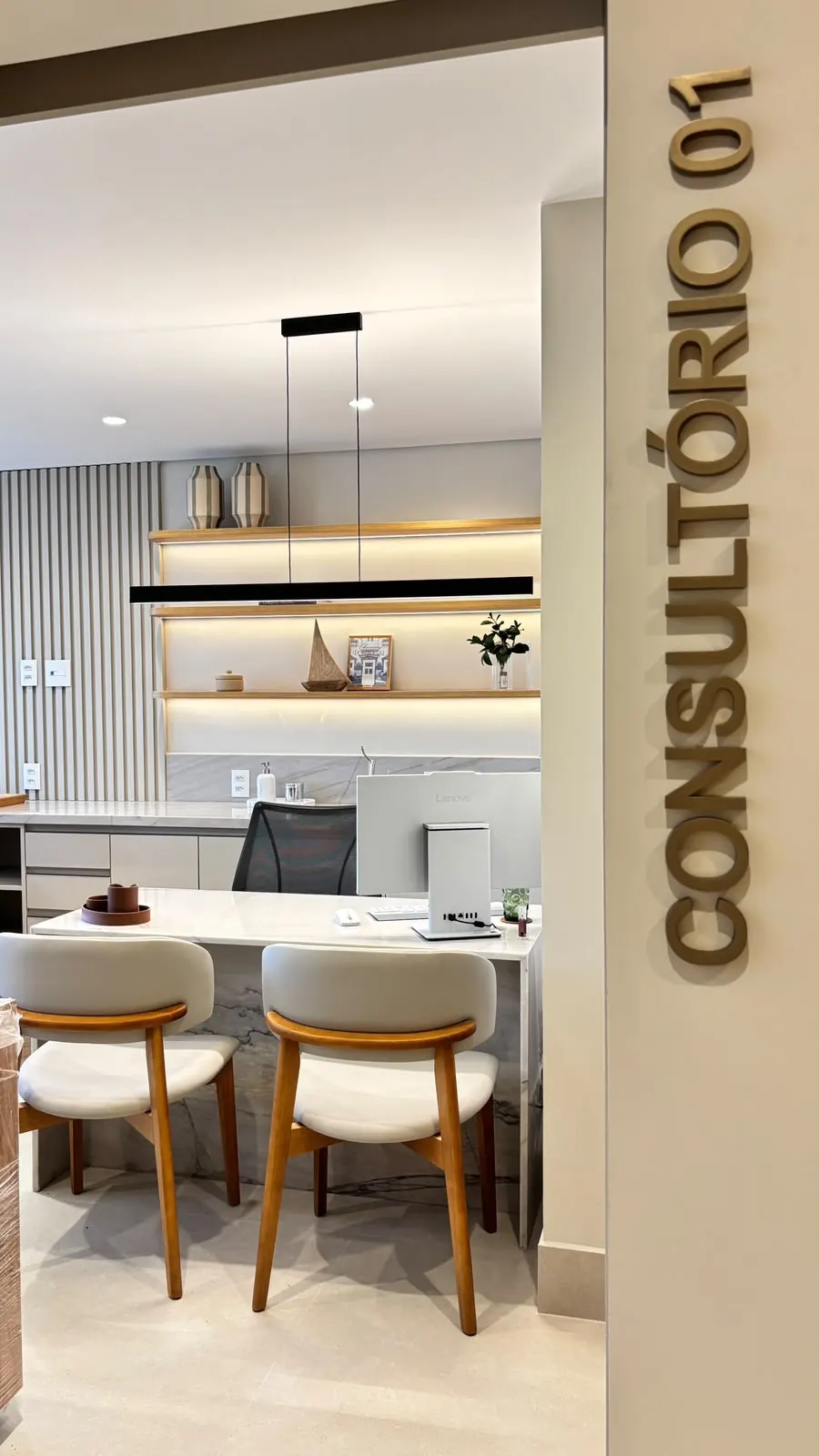 Entrada do Consultório 01, com mesa de atendimento e cadeiras de madeira